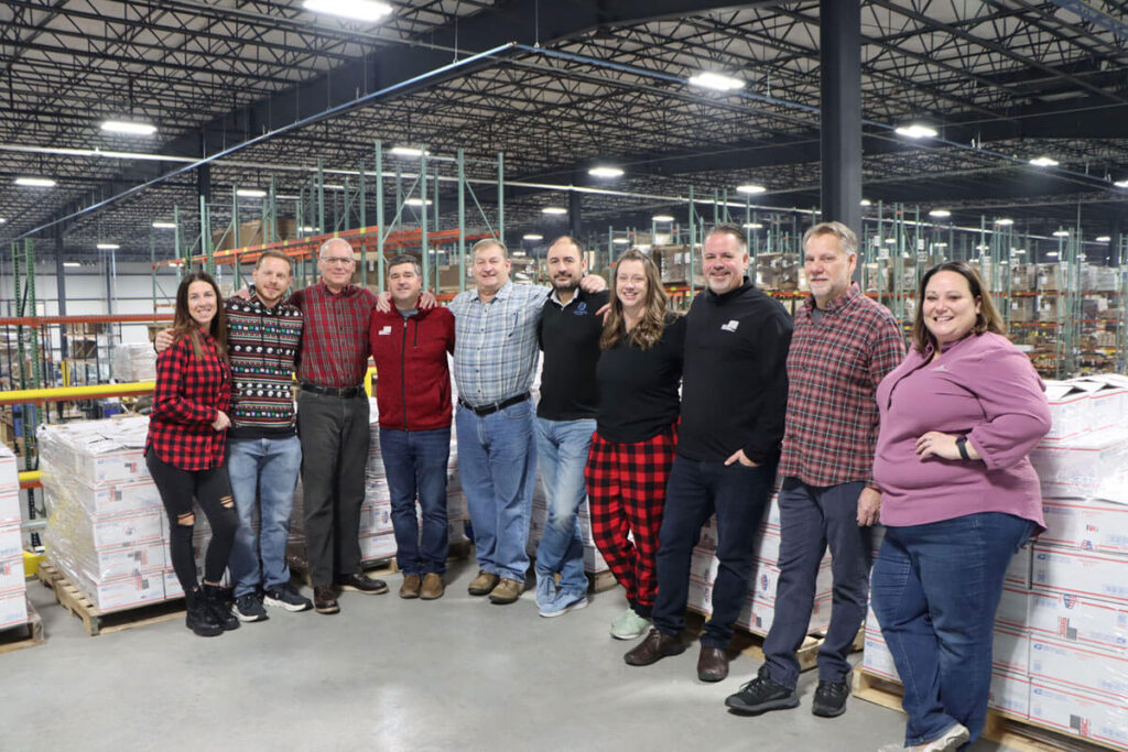 Executive team members lined up in front of filled and packaged boxes for Operation Holiday Drop